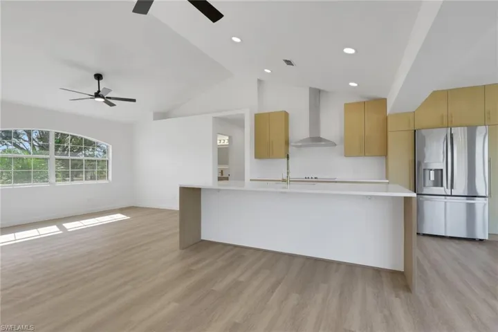 Kitchen featuring stainless steel fridge, modern cabinets, wall chimney exhaust hood, light brown cabinets, and a large island