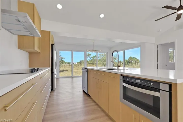 Kitchen featuring light brown cabinets, range hood, a large island, plenty of natural light, and recessed lighting