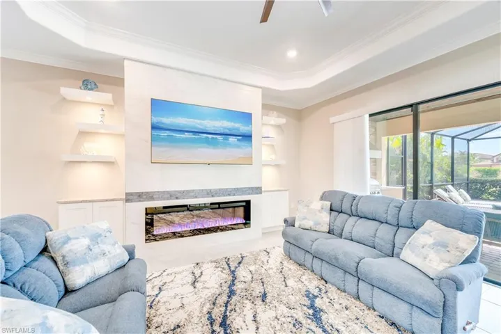 Living area with ornamental molding, built in features, ceiling fan, a tray ceiling, and a glass covered fireplace