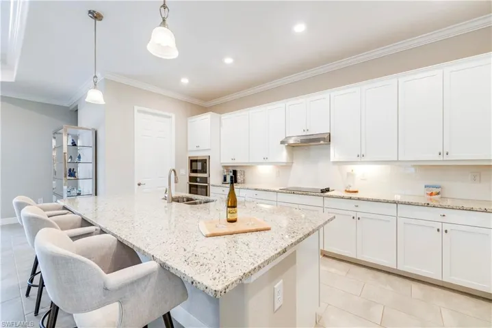 Kitchen with black electric cooktop, under cabinet range hood, light tile patterned flooring, crown molding, and white cabinetry