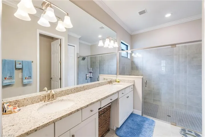 Bathroom featuring a shower stall, a chandelier, tile patterned flooring, double vanity, and ornamental molding