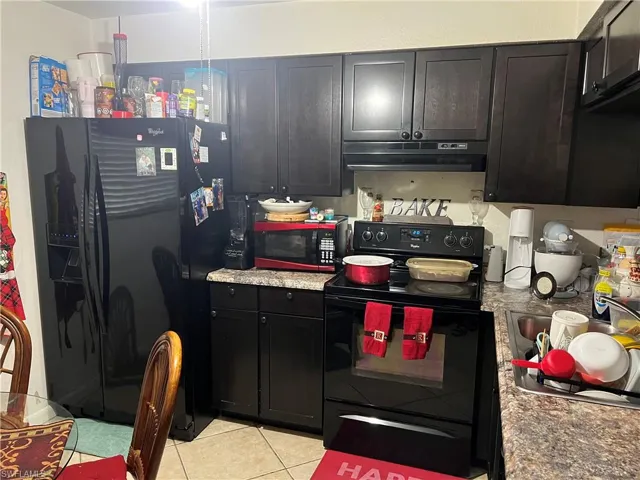 Kitchen featuring black appliances, light tile floors, and range hood