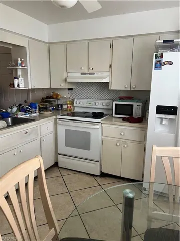 Kitchen featuring fridge, white range with electric stovetop, exhaust hood, light tile floors, and sink