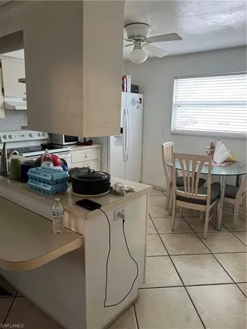 Kitchen featuring exhaust hood, ceiling fan, range, white refrigerator with ice dispenser, and white cabinets