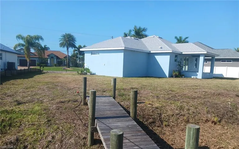 Waterfront property featuring a private wooden dock, a blue-painted exterior, a light gray shingle roof, and a covered patio area