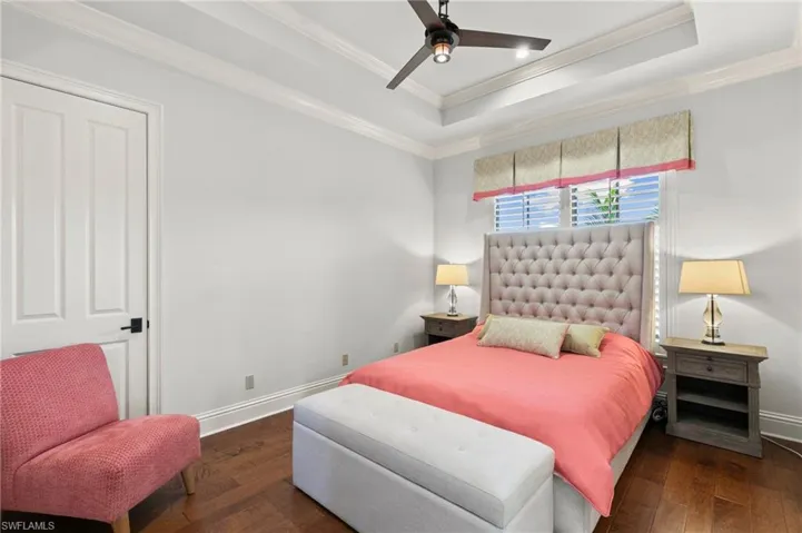 Bedroom featuring ceiling fan, dark hardwood / wood-style flooring, a tray ceiling, and ornamental molding