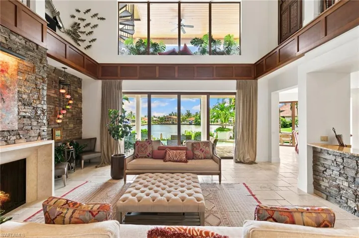 Living room with natural stone flooring, a fireplace, a water view, and a towering ceiling