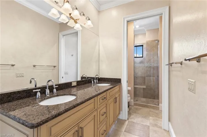 Bathroom featuring tile patterned flooring, a tile shower, dual bowl vanity, toilet, and ornamental molding