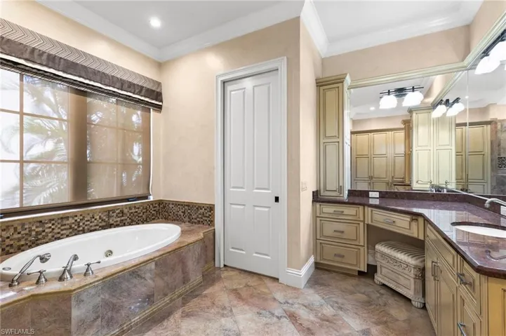 Bathroom featuring vanity, stone floors, tiled bath, and crown molding