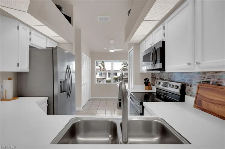 Kitchen with appliances with stainless steel finishes, light tile patterned floors, light countertops, and white cabinetry
