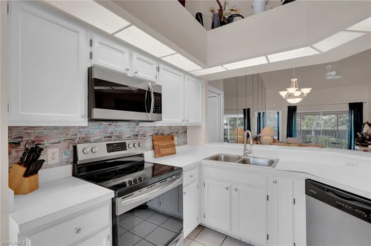 Kitchen with appliances with stainless steel finishes, white cabinets, light tile patterned floors, and decorative backsplash