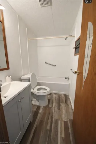 Bathroom with vanity, dark wood-style floors, a textured ceiling, and washtub / shower combination