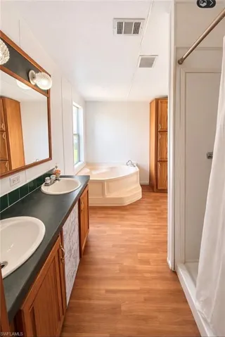 Full bathroom with light wood-style floors, double vanity, a garden tub, and a stall shower