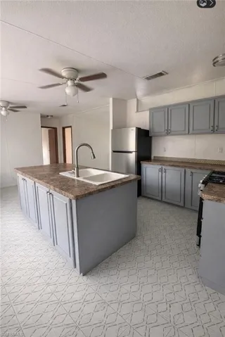 Kitchen featuring light flooring, gray cabinets, an island with sink, a textured ceiling, and freestanding refrigerator
