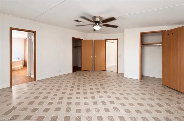 Unfurnished bedroom featuring multiple closets, ceiling fan, light flooring, and ensuite bath