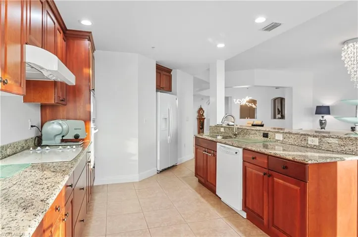 Kitchen with light stone counters, light tile patterned flooring, white appliances, under cabinet range hood, and recessed lighting