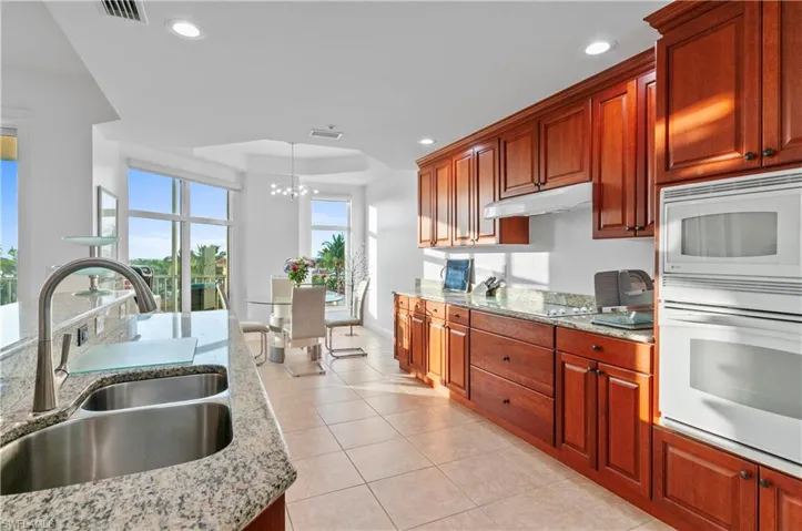 Kitchen with white appliances, light stone counters, decorative light fixtures, a raised ceiling, and light tile patterned flooring
