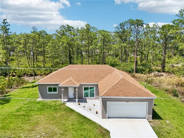 View of front of property featuring stucco siding, an attached garage, a front lawn, concrete driveway, and roof with shingles