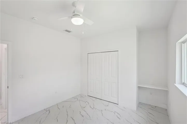 Unfurnished bedroom with light marble finish floors, a closet, baseboards, and ceiling fan