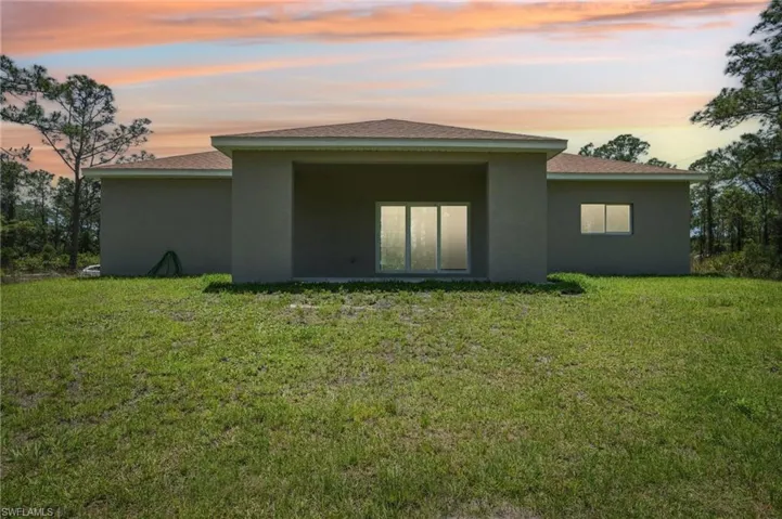 Back of property at dusk featuring stucco siding, a lawn, and roof with shingles