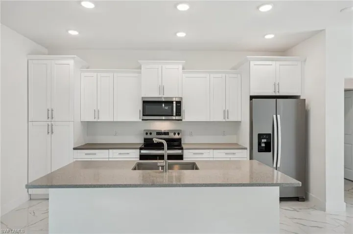 Kitchen with appliances with stainless steel finishes, light marble finish flooring, white cabinets, a kitchen island with sink, and recessed lighting