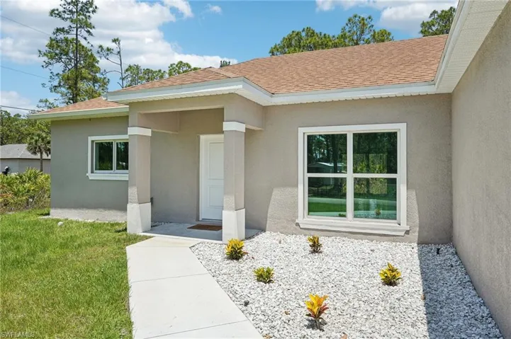 Entrance to property with stucco siding, roof with shingles, and a lawn