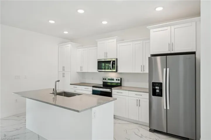 Kitchen featuring appliances with stainless steel finishes, light marble finish flooring, a sink, a kitchen island with sink, and recessed lighting