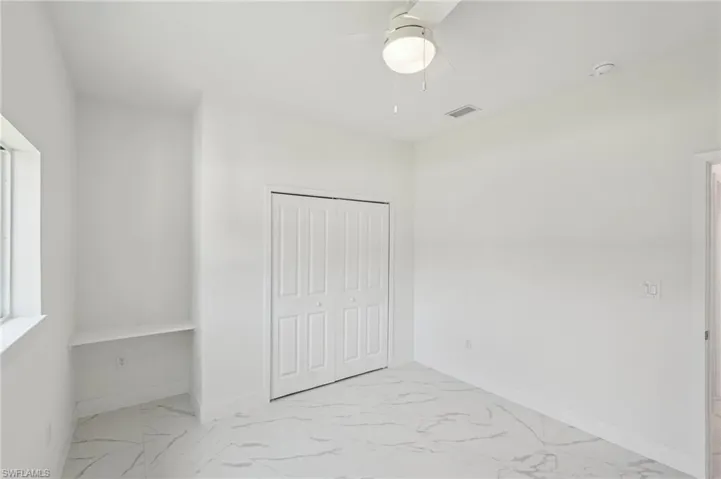 Unfurnished bedroom with light marble finish floors, baseboards, a closet, and a ceiling fan
