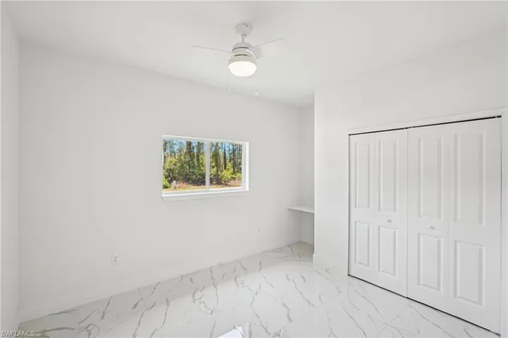 Unfurnished bedroom featuring marble finish flooring, a closet, a ceiling fan, and baseboards