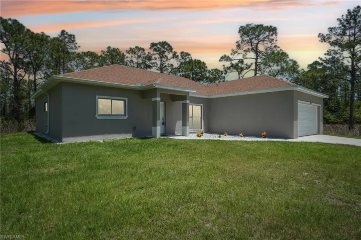 View of front facade featuring stucco siding, an attached garage, a yard, and concrete driveway