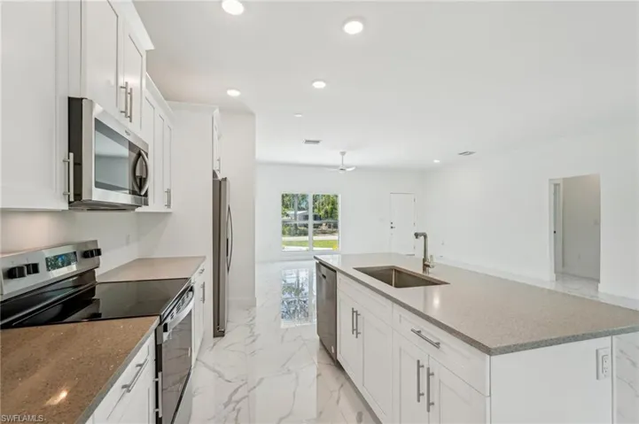 Kitchen with stainless steel appliances, a sink, light marble finish floors, white cabinetry, and recessed lighting