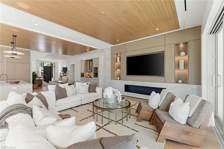 Integrated media wall with built-in shelving, stone fireplace, and wood-finish ceiling accent
