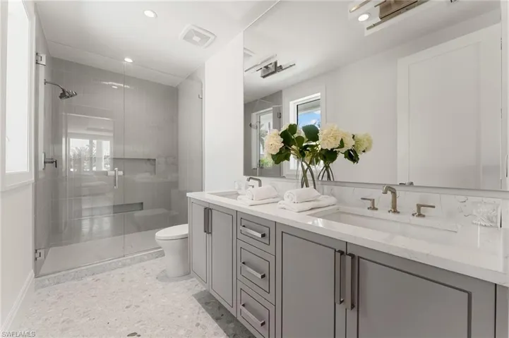 Dual vanity with individual sinks and brushed nickel fixtures, glass-enclosed shower with tiled walls, built-in shower niche, and light gray cabinetry
