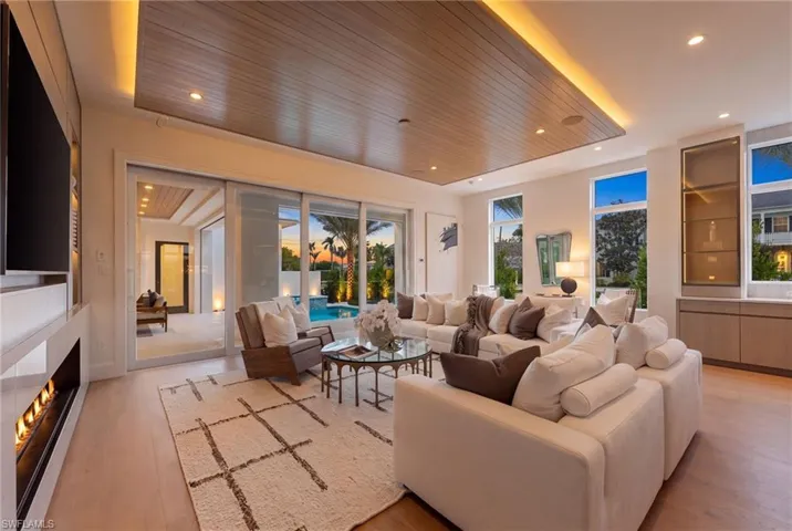 Spacious living area with wood-finish flooring, a linear fireplace, and a wood-paneled ceiling with recessed lighting
