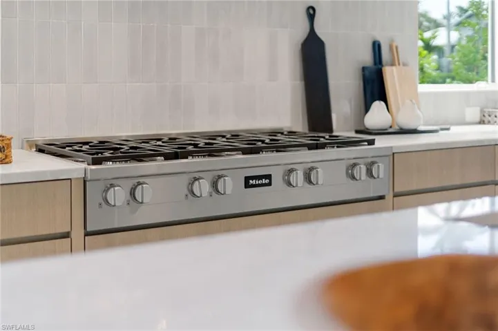 Stainless steel Miele range with six burners, light wood-finish cabinetry, and light-toned vertical tile backsplash