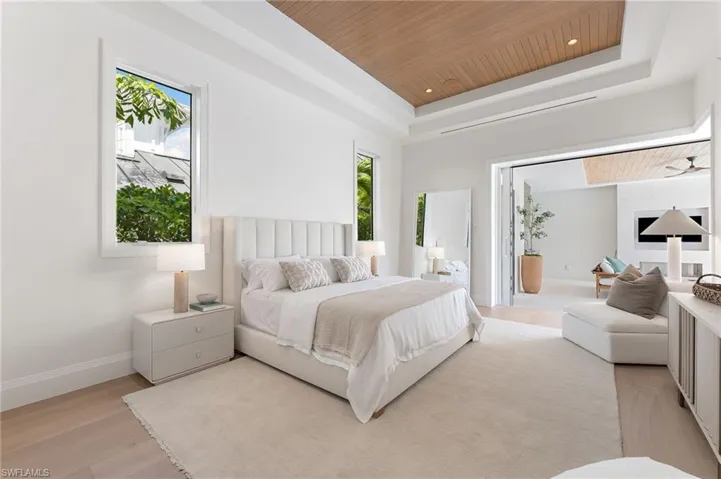 Wood-finish flooring with a light-toned area rug, a tray ceiling featuring a wood-paneled inset, white walls, and a large folding door system