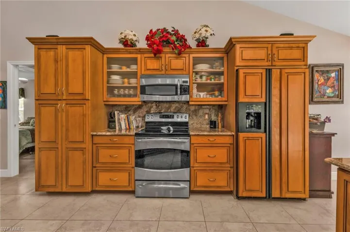 Kitchen featuring backsplash, stainless steel appliances, light stone countertops, light tile patterned flooring, and vaulted ceiling