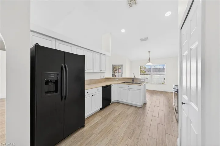 Kitchen featuring black appliances, light countertops, light wood-style flooring, pendant lighting, and white cabinetry