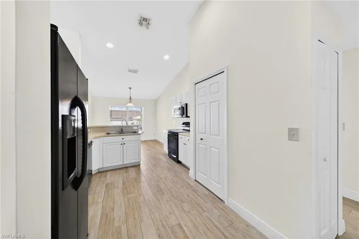 Kitchen featuring light wood-style flooring, black appliances, vaulted ceiling, white cabinetry, and hanging light fixtures