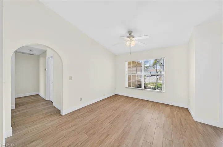 Empty room featuring vaulted ceiling, light wood-style floors, ceiling fan, and arched walkways