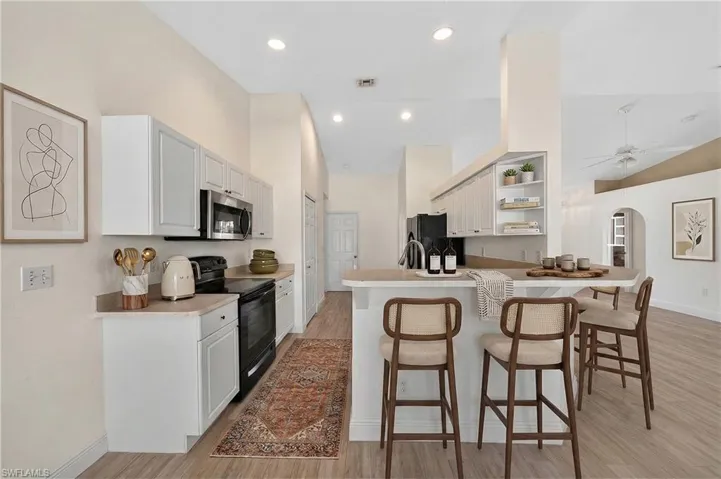 Kitchen with a kitchen breakfast bar, stainless steel appliances, open shelves, arched walkways, and light countertops