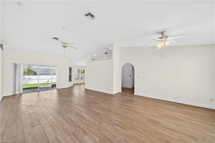 Unfurnished living room with ceiling fan, arched walkways, vaulted ceiling, and light wood-style floors