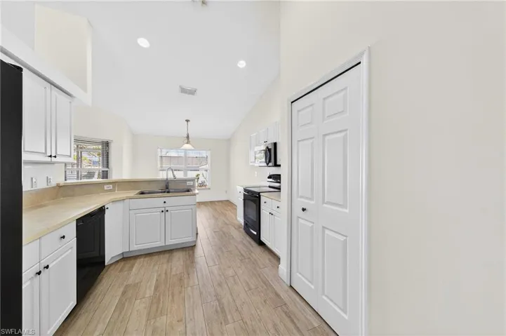 Kitchen with white cabinetry, black appliances, light wood-style floors, light countertops, and vaulted ceiling