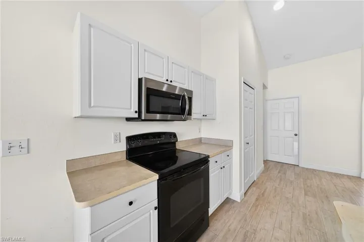 Kitchen featuring black electric range, light countertops, stainless steel microwave, light wood finished floors, and lofted ceiling