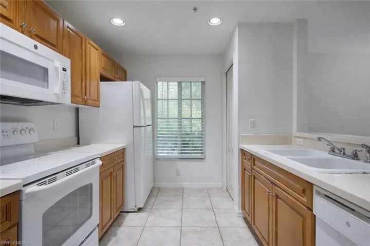 Kitchen featuring white appliances, brown cabinets, light tile patterned floors, and recessed lighting