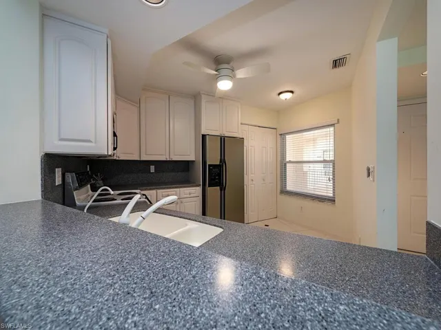 Kitchen featuring white cabinetry, tasteful backsplash, ceiling fan, stainless steel fridge, and sink