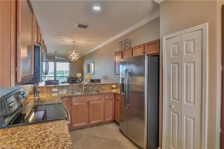 Kitchen with appliances with stainless steel finishes, light stone countertops, decorative light fixtures, sink, and kitchen peninsula
