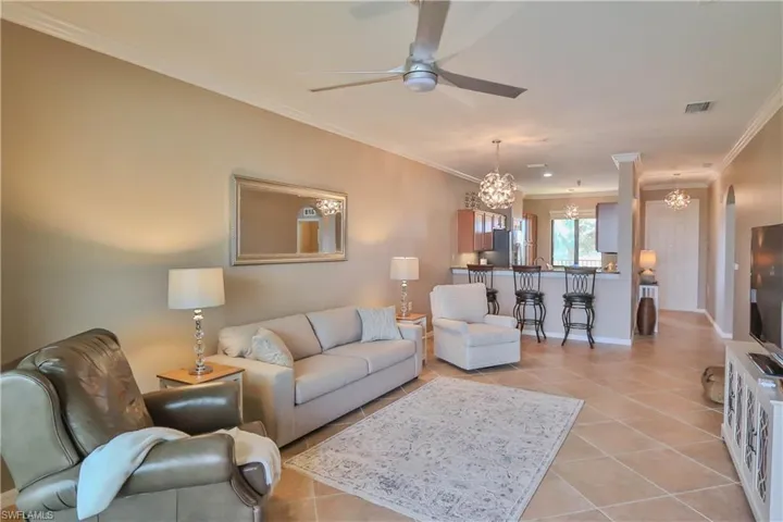 Living room featuring ceiling fan with notable chandelier, light tile patterned floors, and crown molding