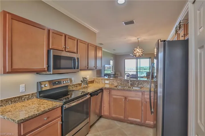 Kitchen featuring kitchen peninsula, sink, ornamental molding, light stone counters, and appliances with stainless steel finishes