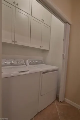 Laundry room featuring light tile patterned floors, washer and clothes dryer, and cabinets